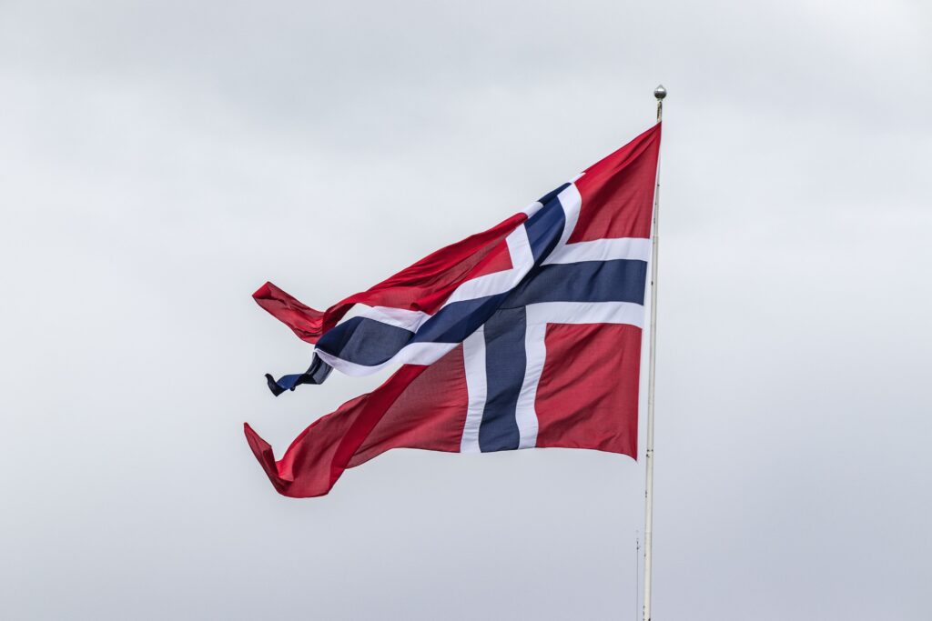 Vibrant Norwegian flag waving on a flagpole against a neutral cloudy sky, symbolizing national pride.